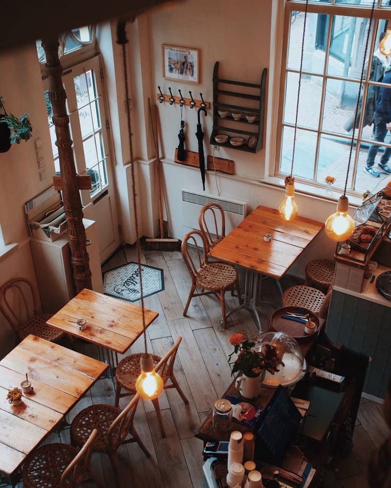 A cosy café seen from above: wooden tables, wicker chairs and warm hanging bulbs